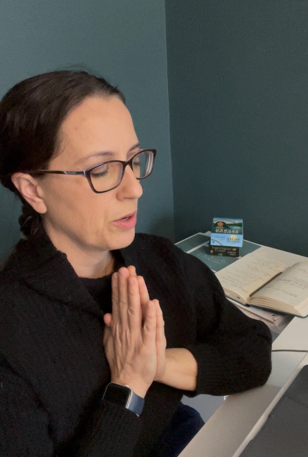 Nicole Beaudin sitting in prayer at her desk, an oracle card deck and open journal behind her